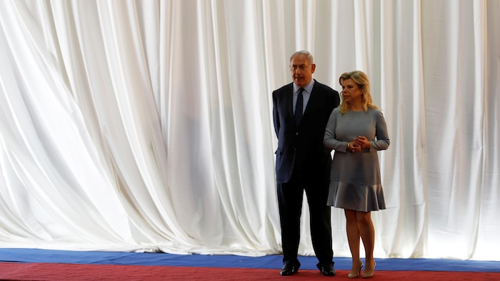 Le premier ministre israélien Benyamin Nétanyahou et sa femme Sara debout sur un tapis rouge et devant un grand rideau blanc.