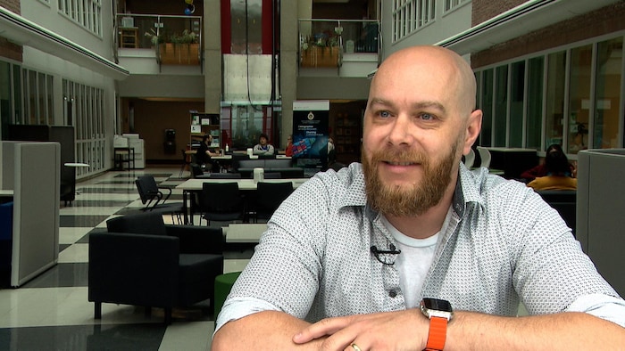 Un homme avec une barbe et souriant est assis à son bureau.