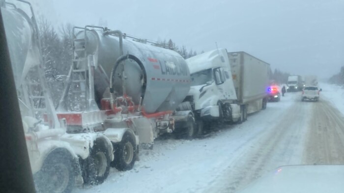 Scène d'un accident de la route impliquant des poids lourds sur une chaussée enneigée.