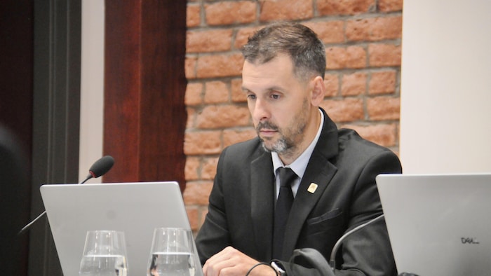 Benoit Forget-Chiasson regarde l'écran de l'ordinateur portable devant lui, à la table du conseil municipal.