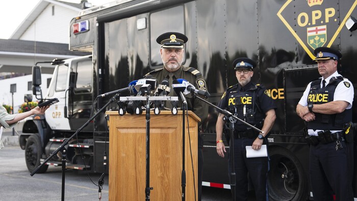 Un policier parle au micro sous le regard de deux de ses collègues devant un camion de la Police provinciale de l'Ontario.