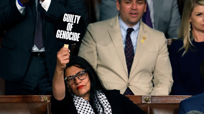 Une femme dans la foule tient haut une petite pancarte.