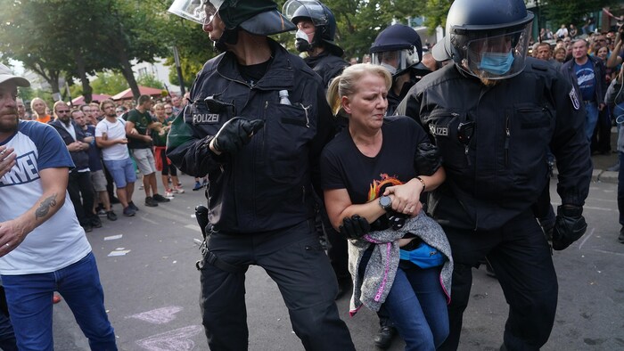 La police antiémeute arrête une femme portant une chemise QAnon.