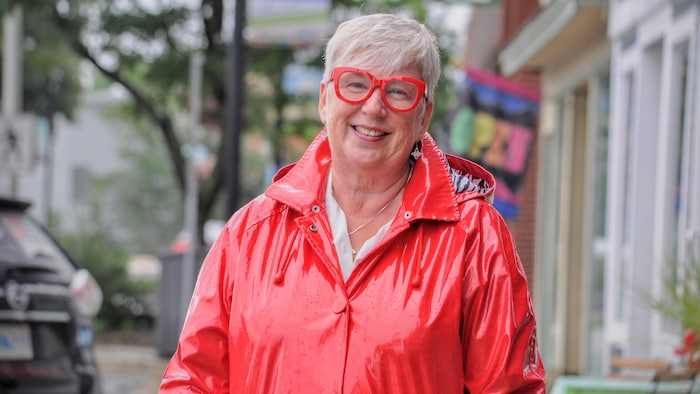 Un femme dans un imperméable rouge sourit pour la caméra.