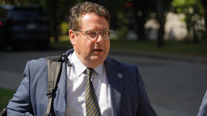 বার্নার্ড ড্রেনভিল তার কাঁধে একটি ব্যাগ বহন করে বাইরে হাঁটেন।