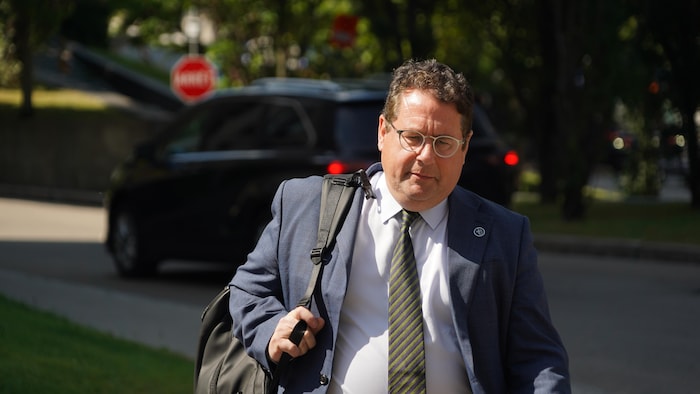 Bernard Drainville, en complet cravate, marche dehors l'air pensif avec un sac sur l'épaule.