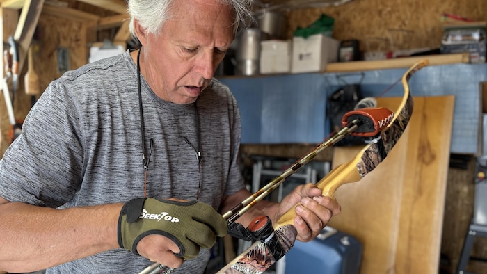 Bernard Jourdain fixe des flèches d'aluminium sur un arc artisanal en bois qu'il a fabriqué.