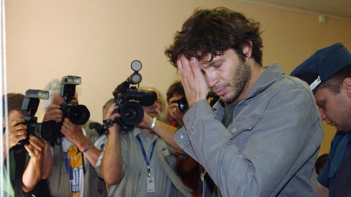 Dans une salle de cour, Bertrand Cantat est entouré de photographes.