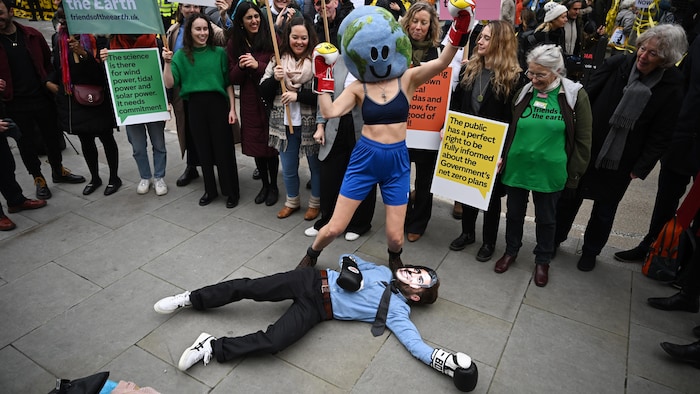 Une manifestation écologiste montre une personne coiffée d'un masque de la Terre triomphant d'un homme au sol.