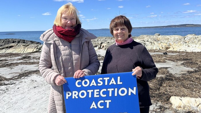 Deux femmes tiennent une pancarte sur laquelle on peut lire "Coastal Protection Act Now".