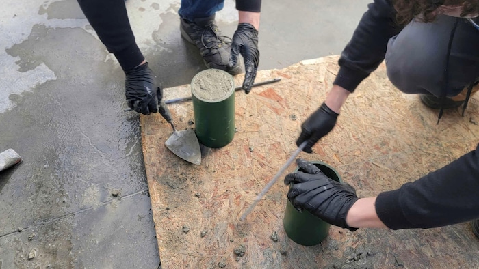 Deux personnes remplissent des cylindres d'essai de béton, sur le sol.