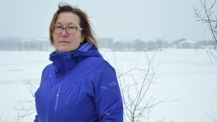 Une femme debout près d'un cours d'eau en hiver.