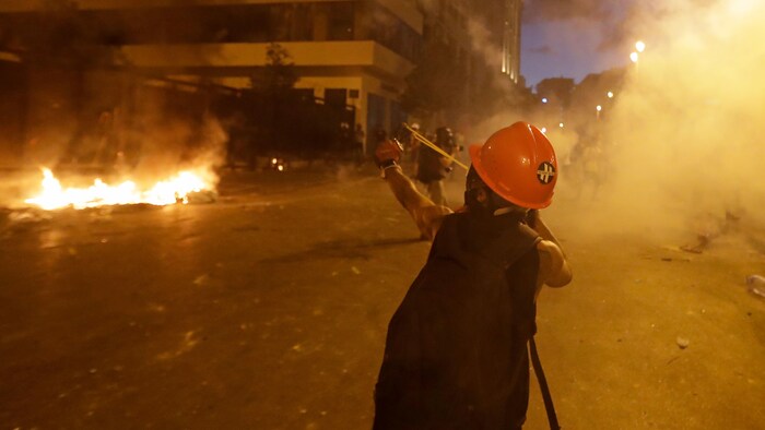 Un manifestant portant un casque de sécurité utilise un lance-pierre dans la rue couverte de fumée de gaz lacrymogène.