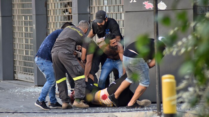 Des hommes tirent un blessé étendu sur le dos sur le sol.