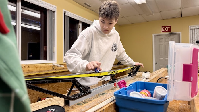 Un jeune homme farte ses skis de fond.
