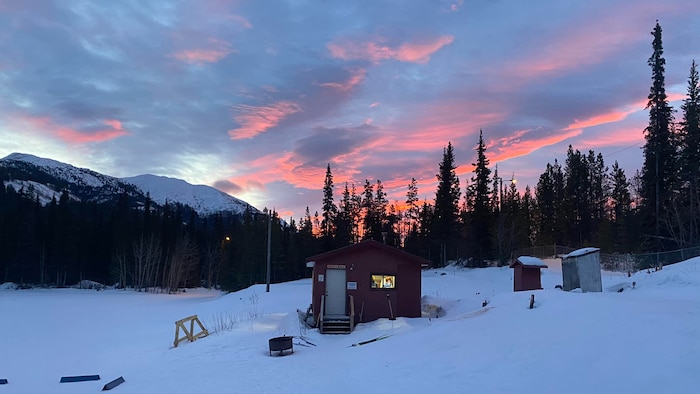 Une maisonnette et des toilettes extérieures sous un coucher de soleil flamboyant.