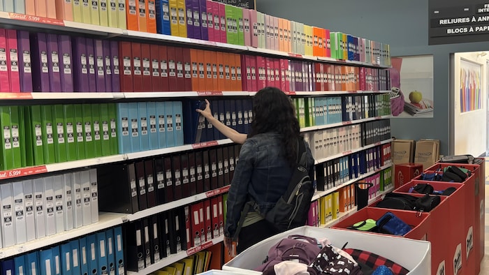 Une femme choisit un cartable dans une rangée de fournitures scolaires.