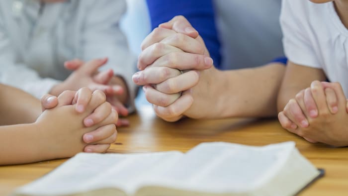 Children praying, hands joined around a Bible.