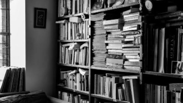 Une bibliothèque remplie à ras bord de livres dans une petite pièce ayant une grande fenêtre.