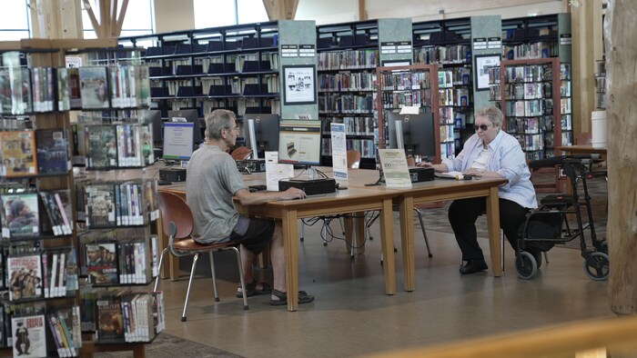 Deux personnes âgées utilisent un ordinateur dans la bibliothèque.