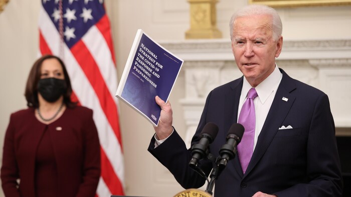 Joe Biden, à la Maison-Blanche, brandissant un document, avec Kamala Harris derrière lui.