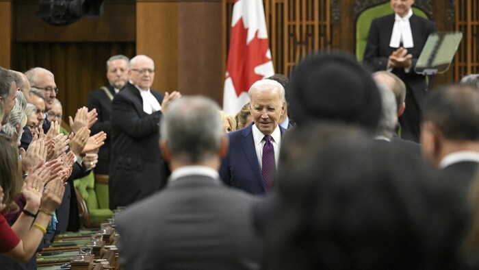 جو بايدن في مجلس العموم الكندي، النوابُ الكنديون من حوله وعلم كندي في عمق الصورة.