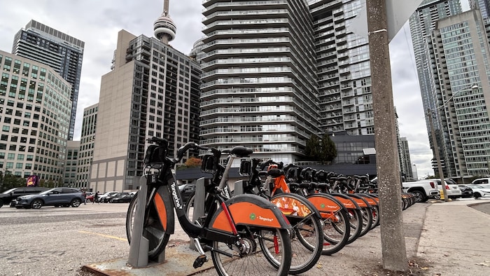 Une rangée de vélo de location dans un stationnement entouré de condominiums et de la Tour CN.