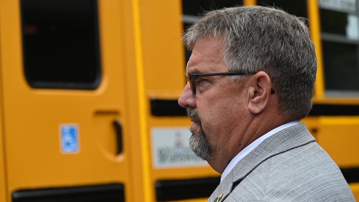 Bill Hogan à l'extérieur, devant un autobus scolaire jaune. 