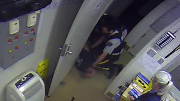 Une image de surveillance dans laquelle on voit un policier donner un coup de genou à un homme plaqué au sol par trois autres policiers.
