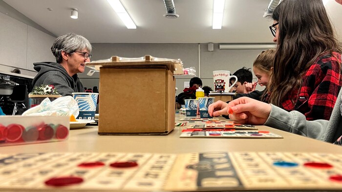 Jeunes et personnes âgées jouent au bingo. Leurs cartes de bingo sont sur des tables. 