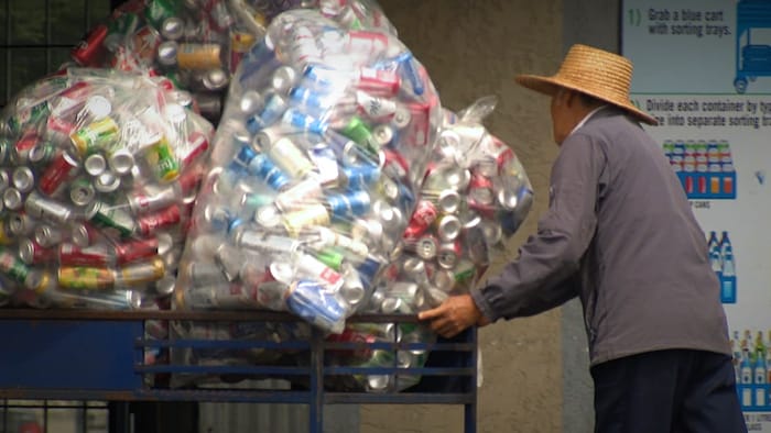 Une personne pousse un chariot avec des sacs de bouteilles vides.