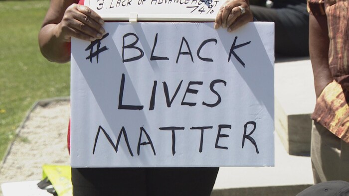Une manifestante tient une pancarte où il est écrit " Les vies des Noirs comptent"