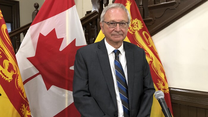 Blaine Higgs devant un micro et entouré de drapeaux du Canada et du Nouveau-Brunswick.