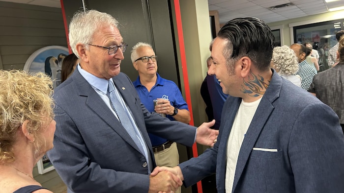 Un homme sert la main d'un autre homme, une foule de gens autour d'eux.