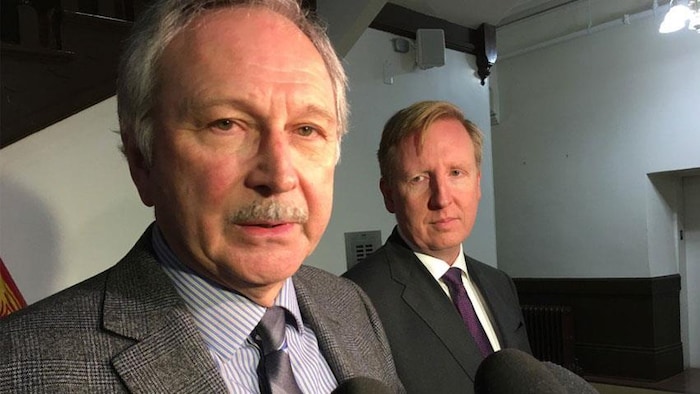 Blaine Higgs parle au micro et Dominic Cardy l'observe de loin.