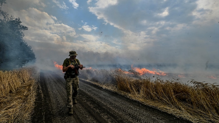 Un soldat ukrainien marche près d'un champ de blé en feu.