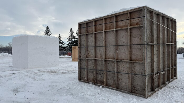 Un grand bloc de neige se tient à côté d'un deuxième bloc entouré de panneaux de bois.