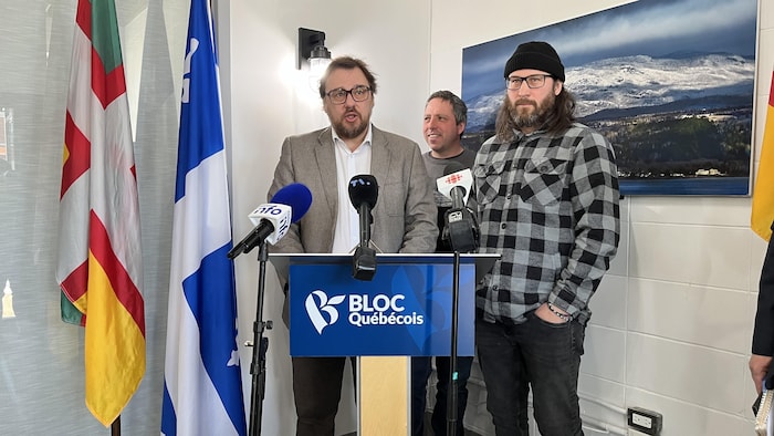 Trois hommes se tiennent derrière des micros lors d'un point de presse.