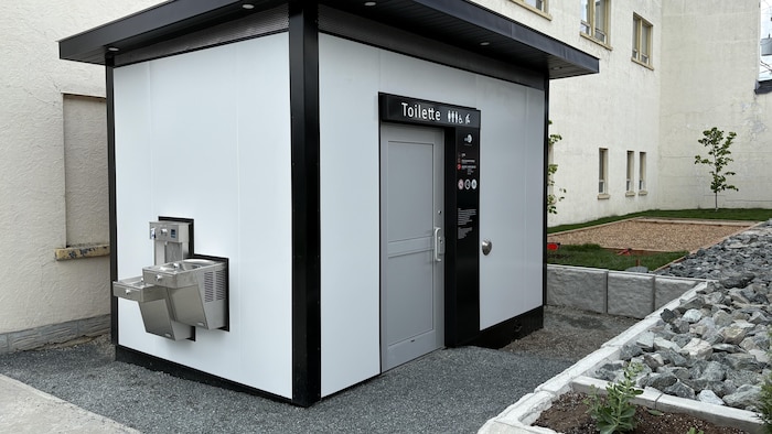 Un bloc sanitaire avec un toilette et un espace pour remplir les gourdes.