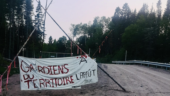 Une banderole au milieu d'un chemin forestier sur laquelle on peut lire : « Gardiens du territoire à l'affût ».