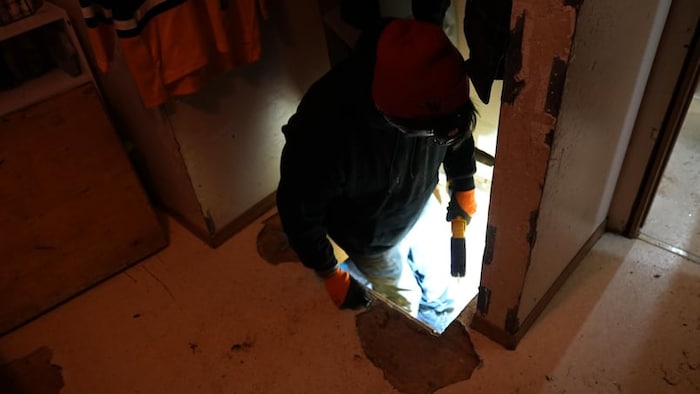 Un homme descend dans un trou, avec des outils électriques en main.