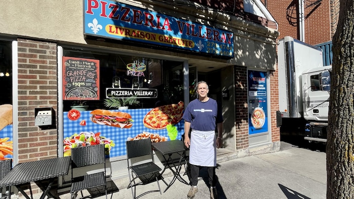Bobby Vergados, devant son commerce qui ressemble à un casse-croûte traditionnel avec des photos de pizza et de sous-marin en devanture.