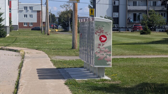 Cinq boîtes aux lettres communautaires de Postes Canada sont alignées à l'extérieur le long du trottoir. 