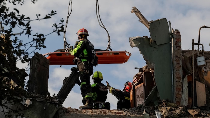 Des secouristes utilisent une grue pour évacuer les corps des personnes retrouvées sous les décombres d'un immeuble d'habitation touché par une frappe aérienne russe.