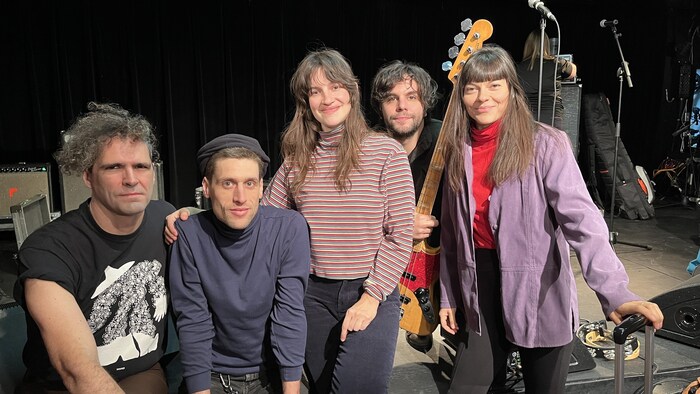 Cinq personnes posent devant une scène où sont visibles des instruments.