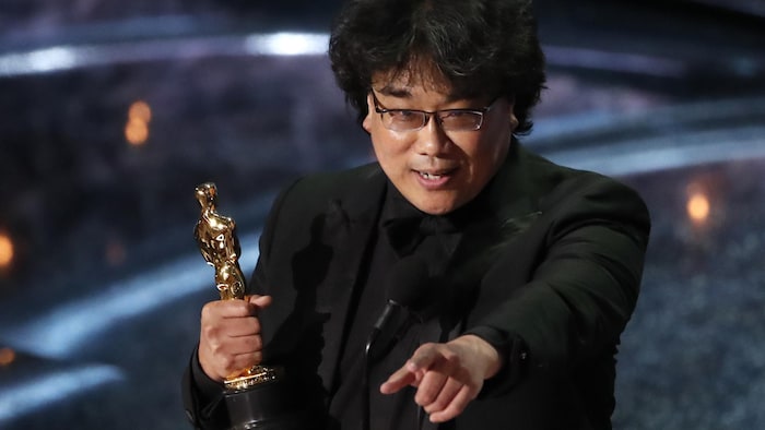 Un homme sur scène tient l'Oscar dans sa main droite et pointe la salle de sa main gauche.