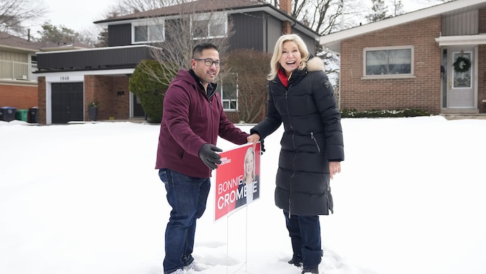 Alvin Tedjo plante une pancarte sur une pelouse en compagnie de Bonnie Crombie.
