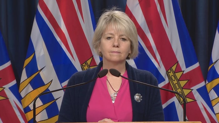 Bonnie Henry sa harap ng mikropono at nasa likuran niya ang watawat ng British Columbia.