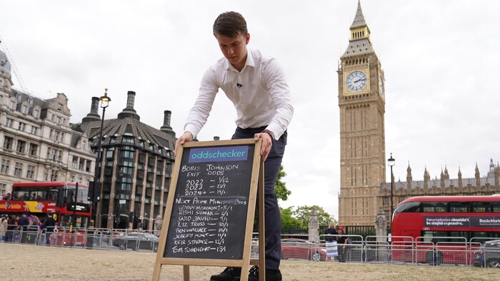 Un homme installe un chevalet sur lequel on peut lire des cotes devant le parlement britannique. 
