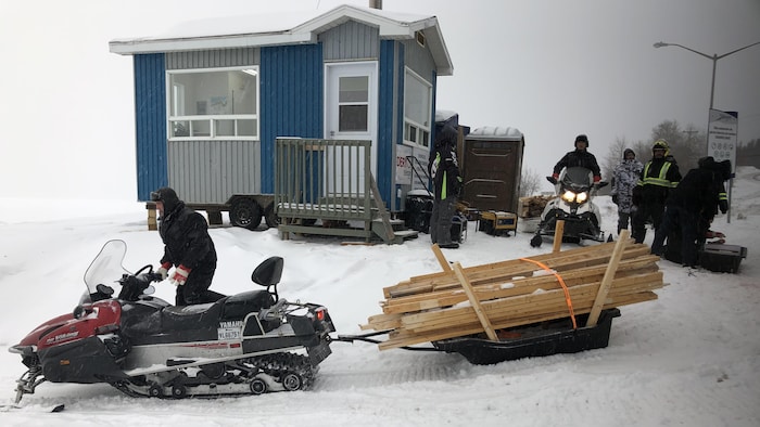 Un motoneigiste transporte des planches de bois sur la glace.